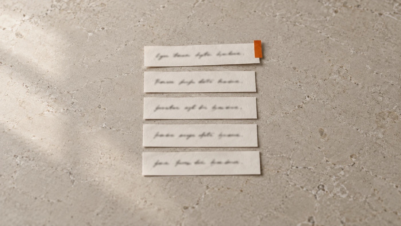 Five strips of paper with one line of handwriting each, laid in a column on a stone desk, the top one marked with an orange tab.