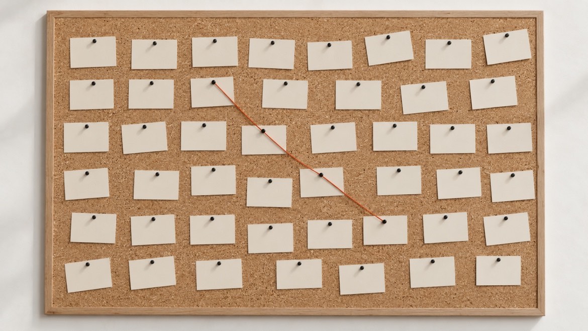 A cork board covered in blank index cards, with an orange thread connecting just four of them.